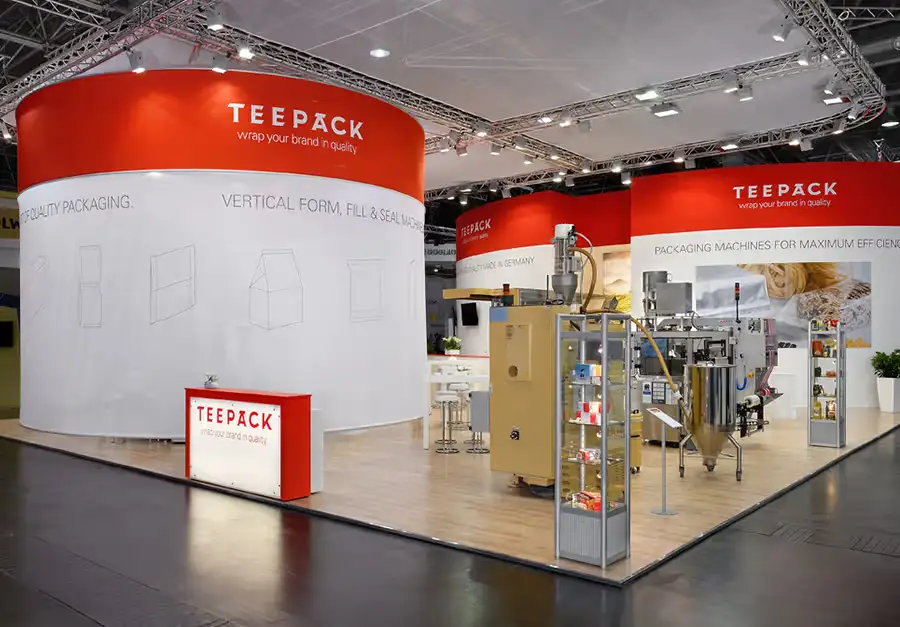 Messestand Teepack – Lüco Messebau Von Lüco gebauter Messestand für Teepack mit runden Turmelementen und ausgestellter Verpackungsmaschine